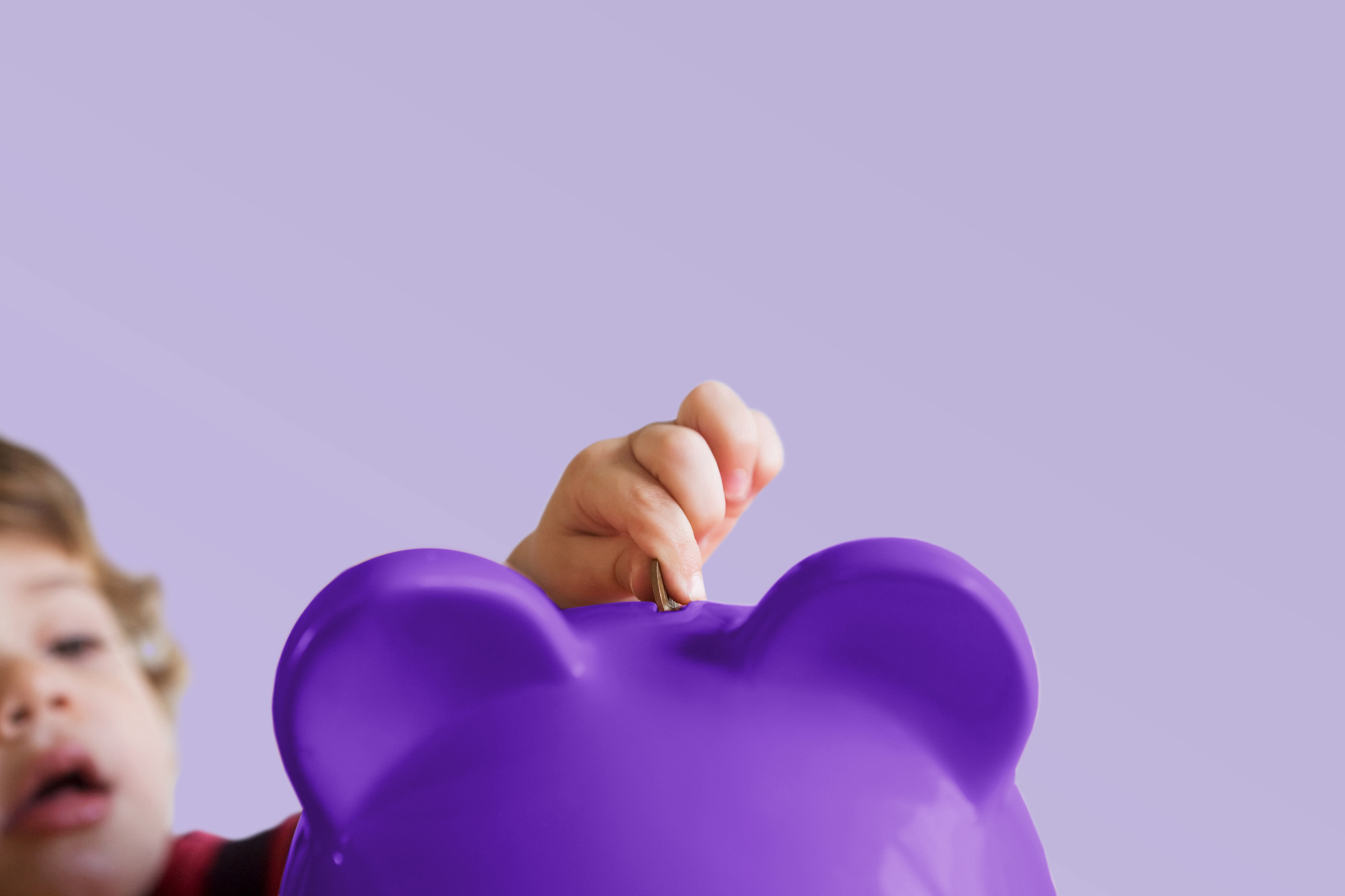 Kind wirft Geld in ein violett abgeschnittenes Sparschwein - Landscape Kind wirft Geld in ein violett abgeschnittenes Sparschwein - Landscape